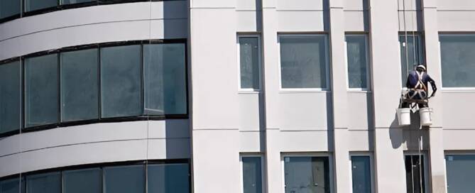 Commercial painter applying exterior coating on a modern office building facade with clean lines