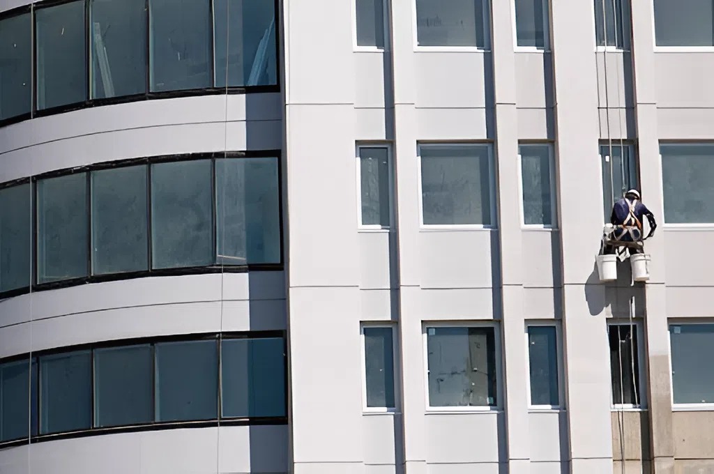 Commercial painter applying exterior coating on a modern office building facade with clean lines