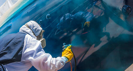Industrial painting contractor applying protective coating to a large industrial surface with spray equipment and safety gear