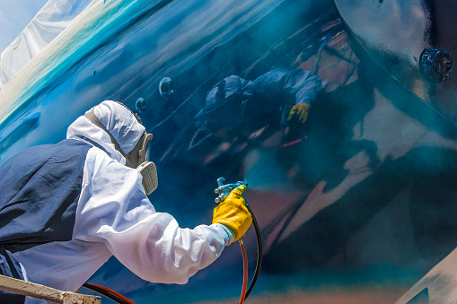 Industrial painting contractor applying protective coating to a large industrial surface with spray equipment and safety gear
