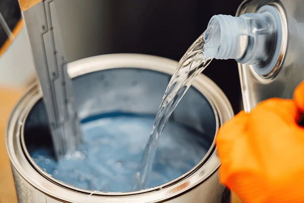 Pouring industrial paint solvent into a metal container with protective gloves for coating preparation