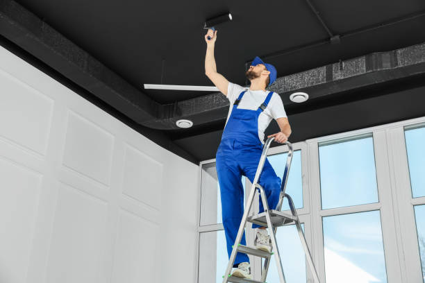: Commercial painter standing on a ladder while applying paint to a ceiling in a modern interior space